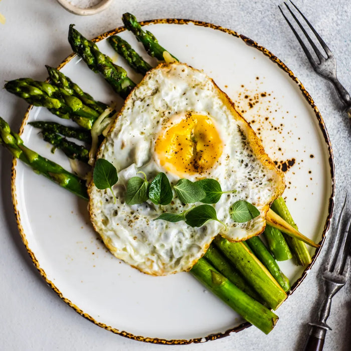 Assiette d'asperges poêlées accompagnées d'un œuf au plat sur un lit de mâche