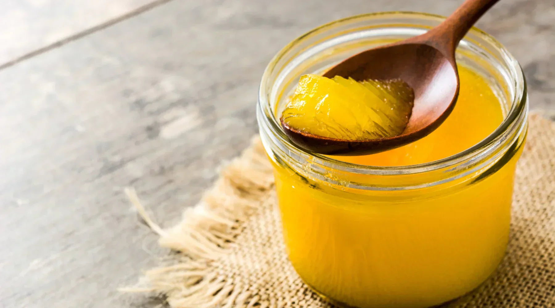 Pot de ghee maison avec une cuillère en bois, montrant sa texture dorée et fondante. Beurre clarifié utilisé en cuisine ayurvédique et pour la cuisson à haute température.