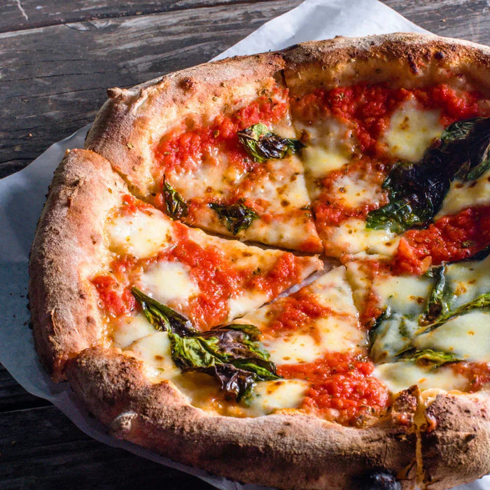 Pizza Margherita artisanale à la croûte dorée et gonflée, garnie de mozzarella fondante, de tomates San Marzano et de basilic frais, servie sur une table rustique en bois. Symbole de la tradition napolitaine et de l’authenticité italienne.