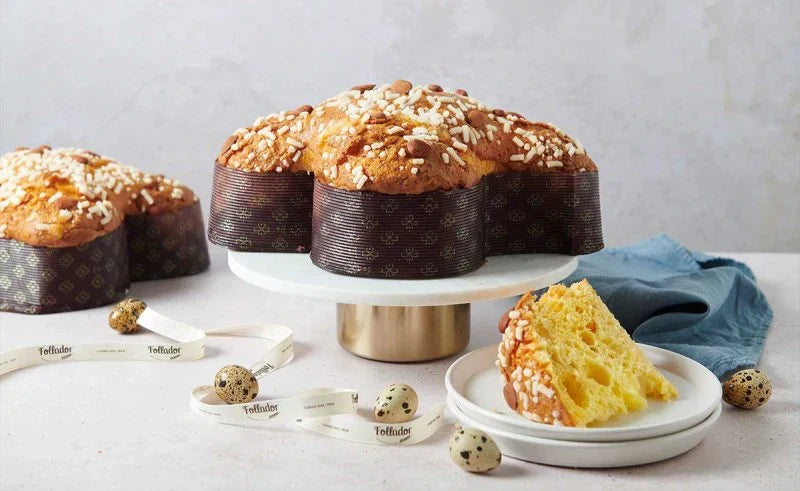 Un artisan tenant délicatement une colomba traditionnelle garnie à la main, avec un glaçage croquant et des éclats d’amandes, prête à être dégustée pour les fêtes de Pâques.