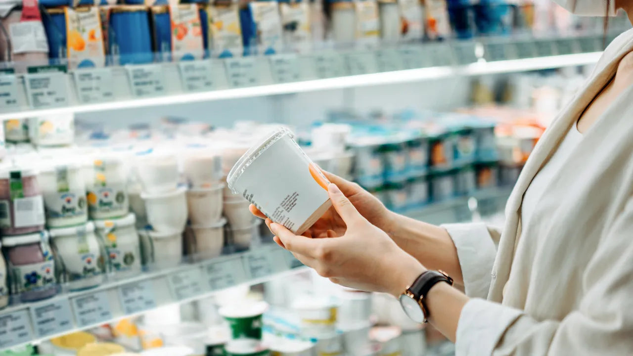Consommatrice tenant un produit au rayon frais, en train de lire l’étiquette alimentaire dans un supermarché