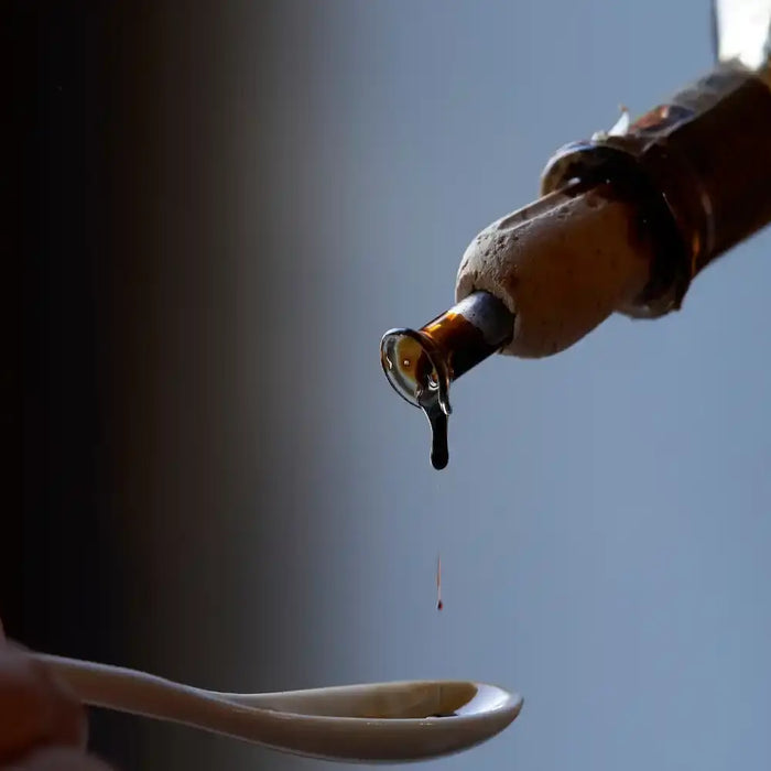 Goutte de vinaigre balsamique tombant d’une bouteille dans une cuillère, symbole de tradition et raffinement italien.