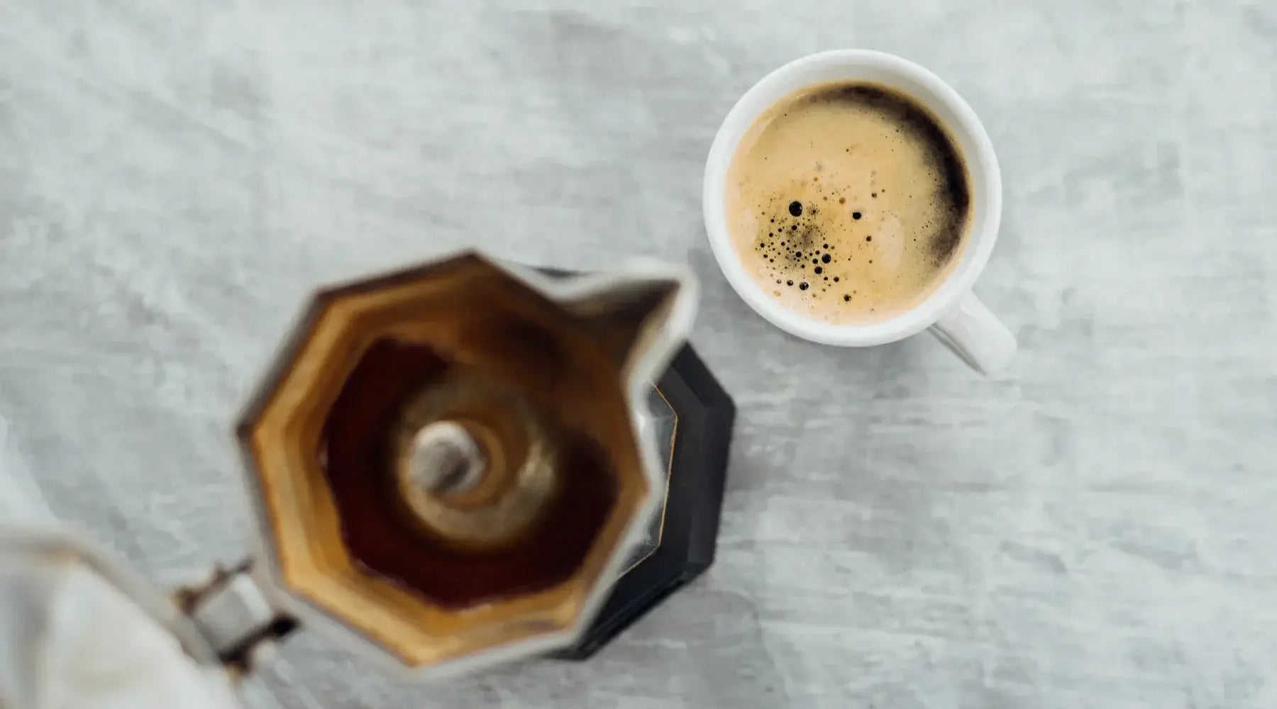 Vue du dessus d’une cafetière italienne moka et d’une tasse de café crémeux sur une table claire — le rituel du café à l’italienne.