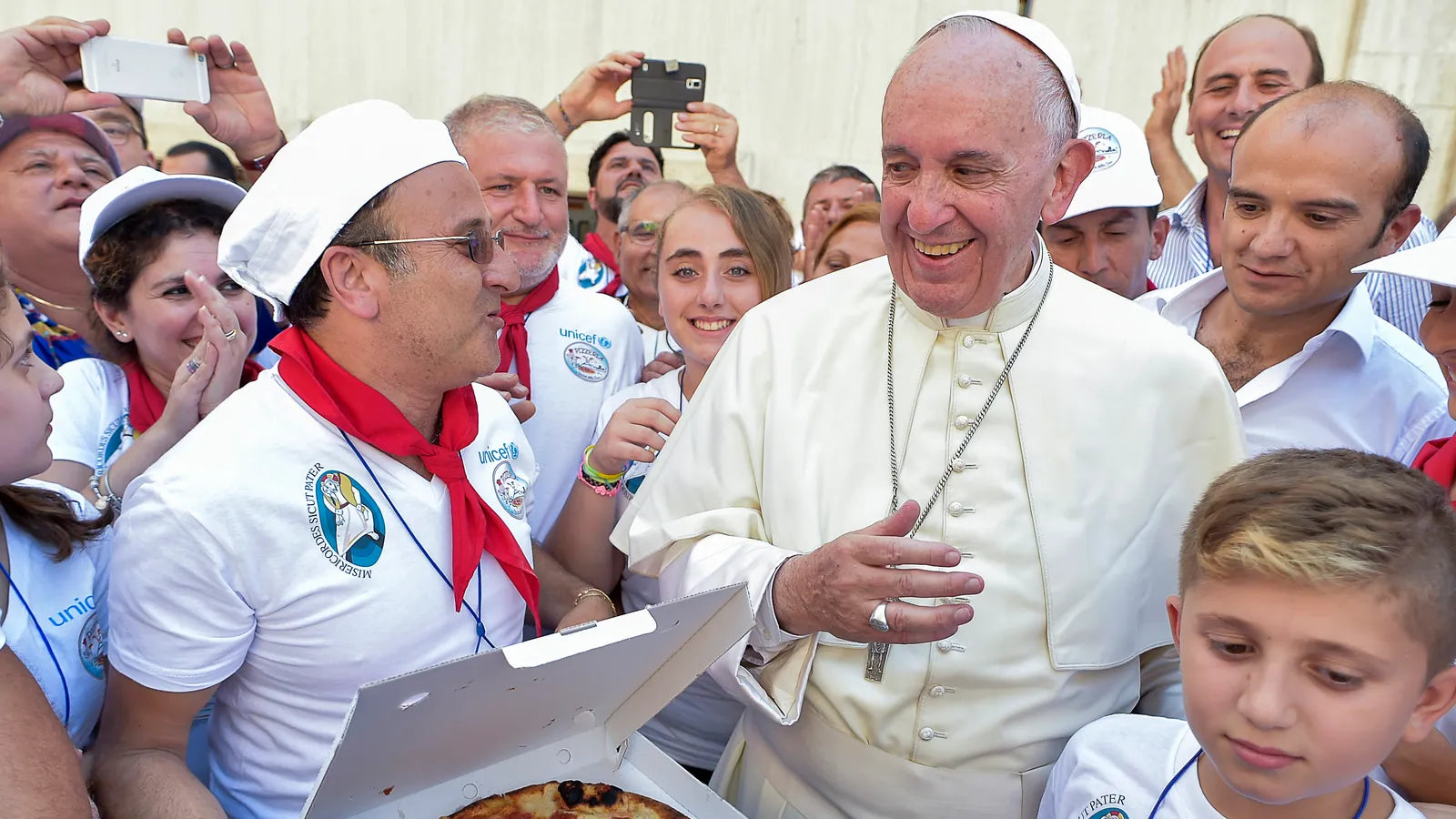 Le Pape François souriant, entouré d’une foule de fidèles et de pizzaiolos, recevant une pizza artisanale lors d’un événement spécial au Vatican