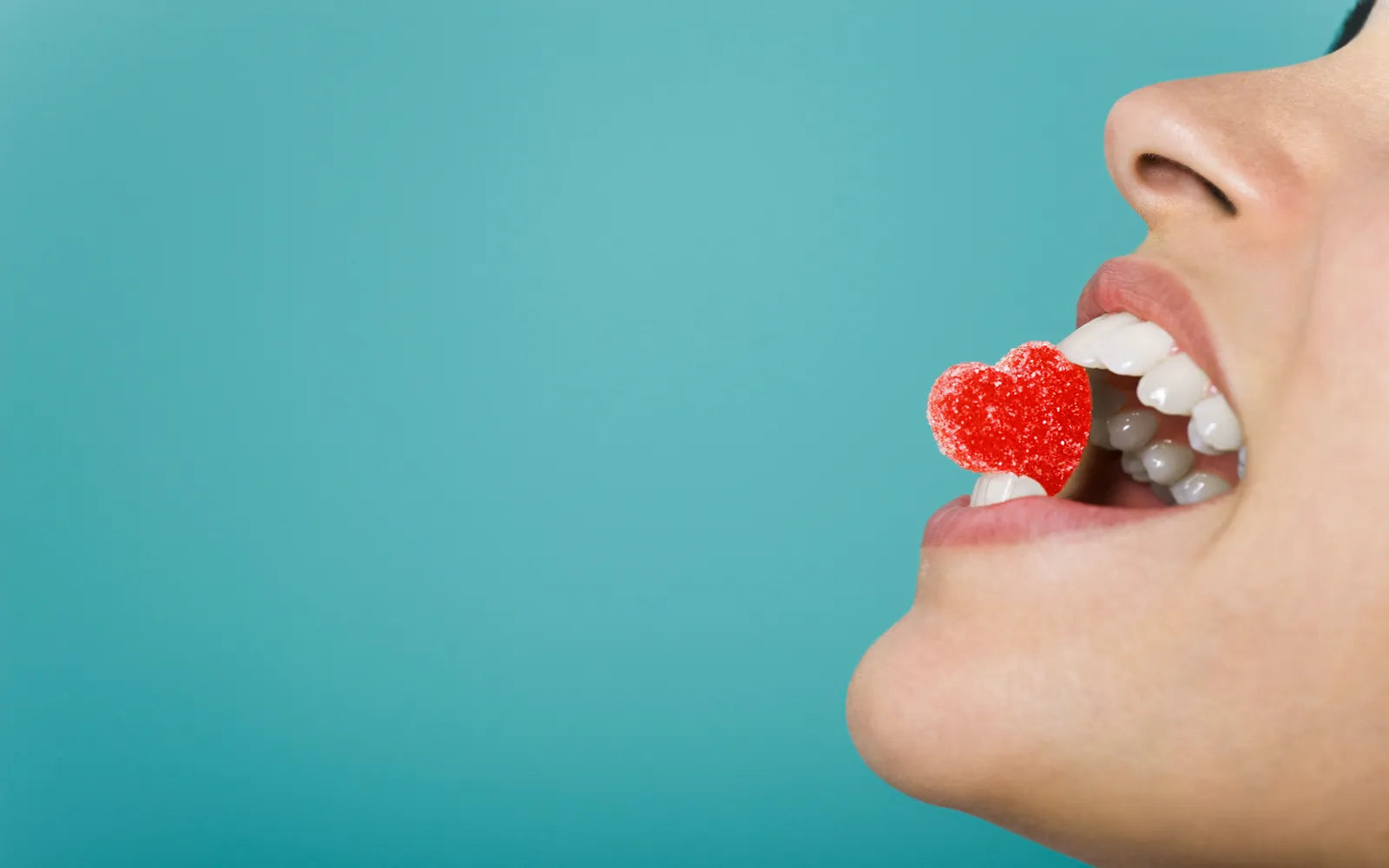 Femme croquant une sucrerie en forme de cœur, symbole de l'impact de l'alimentation sur la santé dentaire