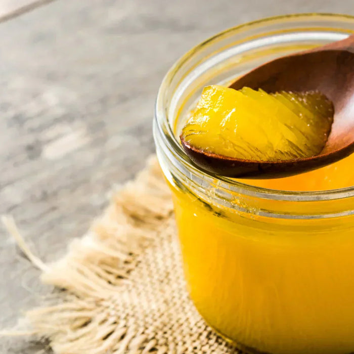 Pot de ghee maison avec une cuillère en bois, montrant sa texture dorée et fondante. Beurre clarifié utilisé en cuisine ayurvédique et pour la cuisson à haute température.