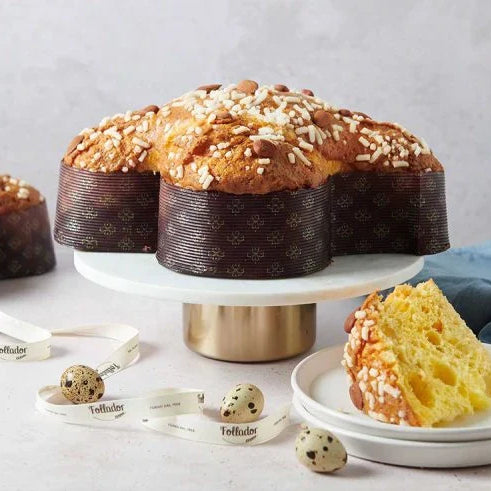 Un artisan tenant délicatement une colomba traditionnelle garnie à la main, avec un glaçage croquant et des éclats d’amandes, prête à être dégustée pour les fêtes de Pâques.