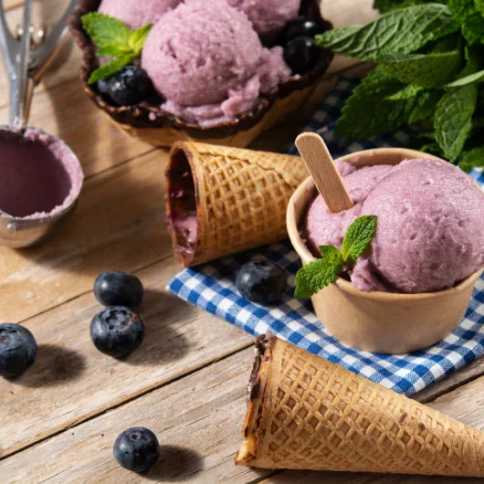 Glace keto aux myrtilles sans sucre ni gluten, servie en cornet et en pot sur table rustique