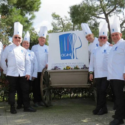 Chefs fondateurs de la CICA-E en tenue blanche avec toques, posant autour du logo de la confédération italienne des cuisiniers et artisans de l’enogastronomie