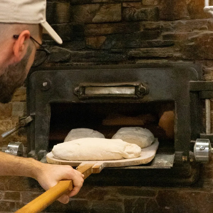 Un boulanger enfournant du pain artisanal dans un four traditionnel en pierre chez Eataly Smeraldo, illustrant le processus de cuisson du pain au levain.