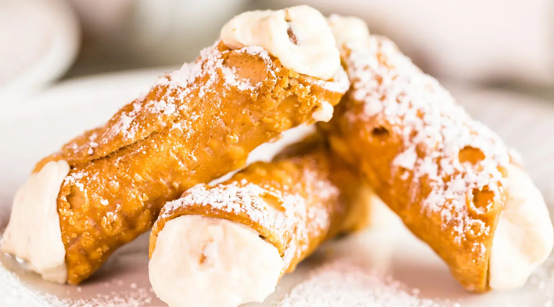 Cannoli siciliens traditionnels faits maison, garnis de crème à la ricotta et saupoudrés de sucre glace, servis sur une assiette blanche.