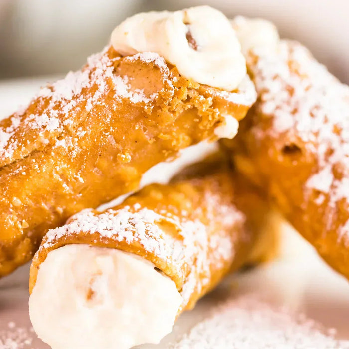 Cannoli siciliens traditionnels faits maison, garnis de crème à la ricotta et saupoudrés de sucre glace, servis sur une assiette blanche.