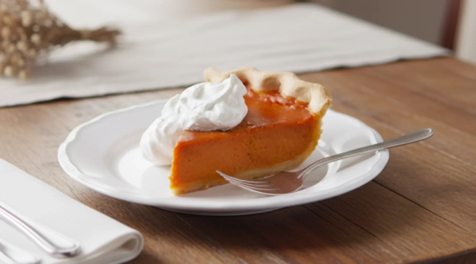 Tarte à la citrouille américaine servie sur une assiette blanche, garnie de crème fouettée, posée sur une table en bois — dessert crémeux et parfumé à la cannelle, typique d’Halloween et de Thanksgiving.