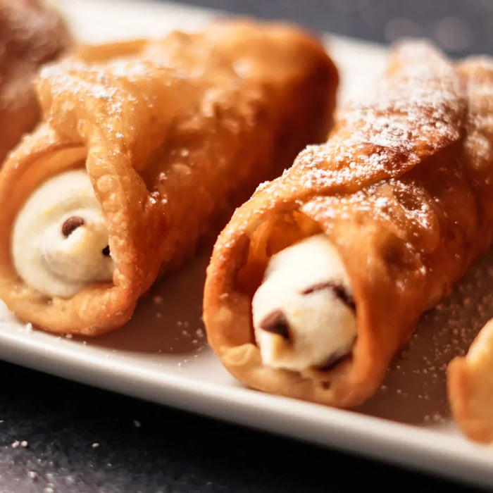 Cannoli italiens authentiques garnis de ricotta et pépites de chocolat, disposés sur une assiette blanche, saupoudrés de sucre glace.