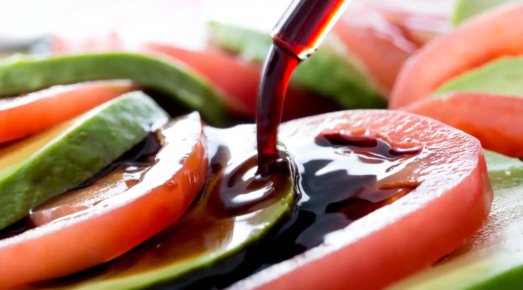 Tranches de tomates et d’avocats nappées de vinaigre balsamique versé délicatement.