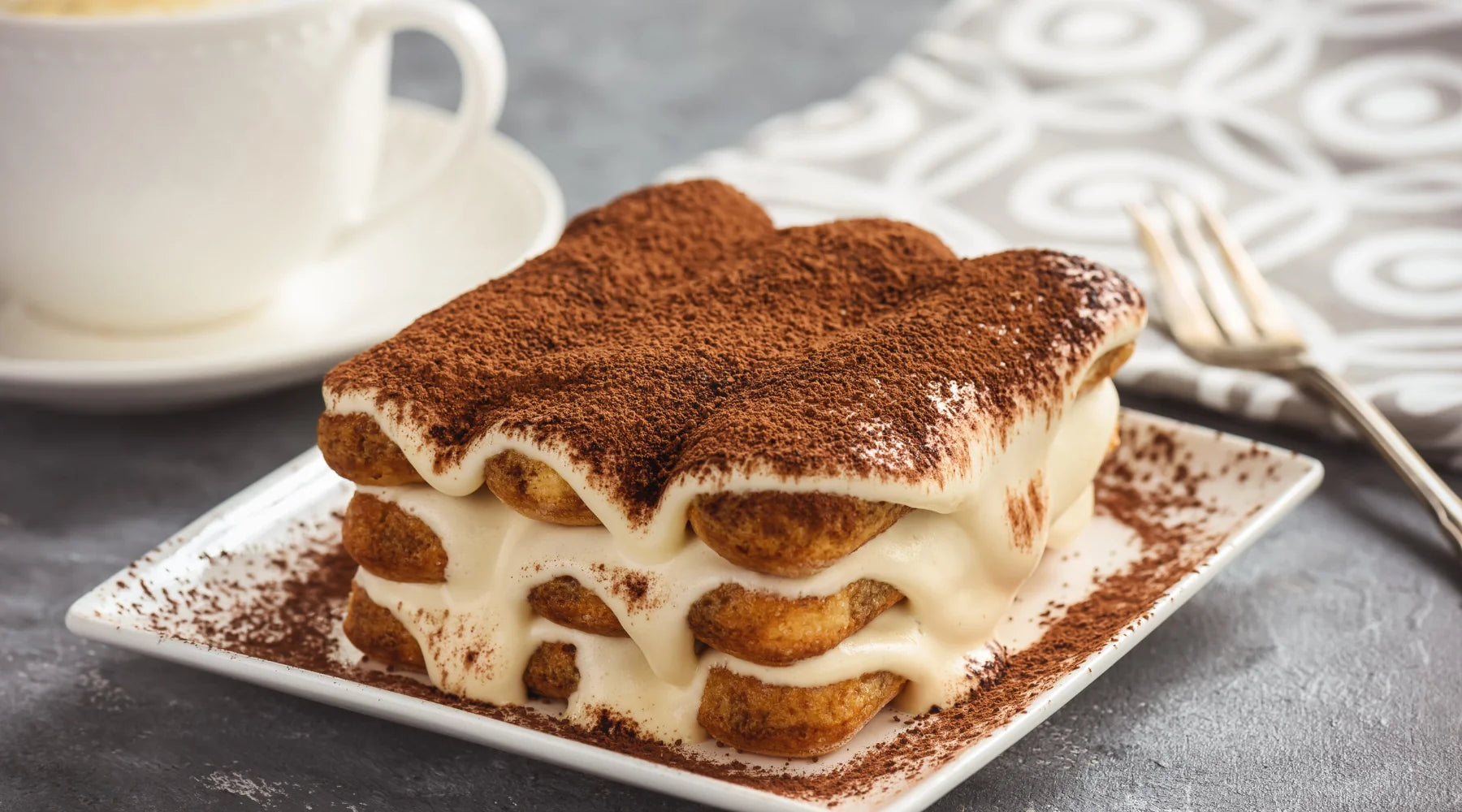 Part de tiramisù crémeux saupoudré de cacao sur une assiette, illustrant un dessert traditionnel italien