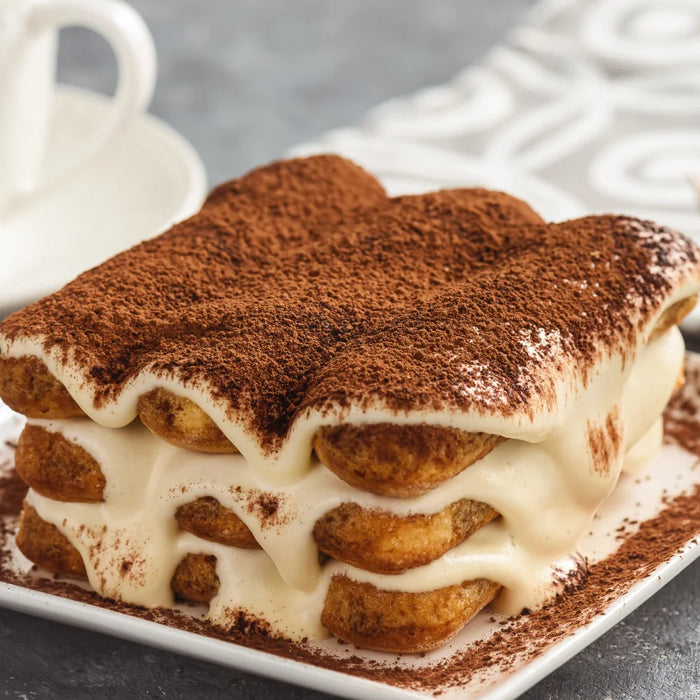 Part de tiramisù crémeux saupoudré de cacao sur une assiette, illustrant un dessert traditionnel italien