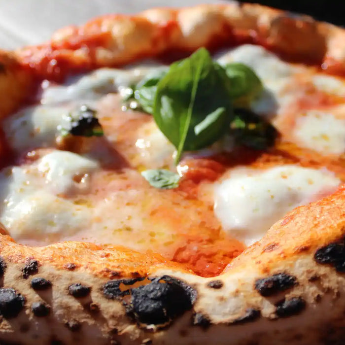 Pizza napolitaine artisanale avec mozzarella fondue, basilic frais et pâte à bord doré.
