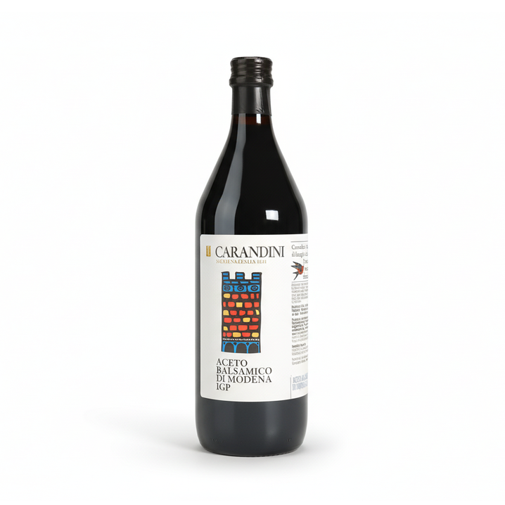 Bouteille en verre foncé bordelaise d'Aceto Balsamico di Modena IGP de la maison Carandini, fondée en 1860 à Modène, Italie — étiquette blanche illustrée de barriques traditionnelles en rouge, jaune et bleu, symbole du processus d'affinage en fûts de bois.