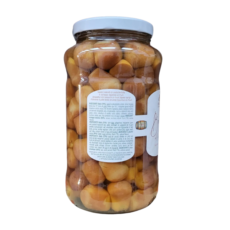 Baba au rhum en bocal avec étiquette latérale détaillant les ingrédients et les instructions, vue sur la transparence des babas imbibés de sirop.